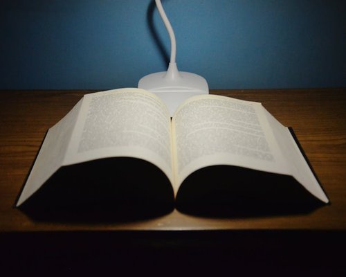 A well placed reading lamp illuminating an open book on a wooden desk
